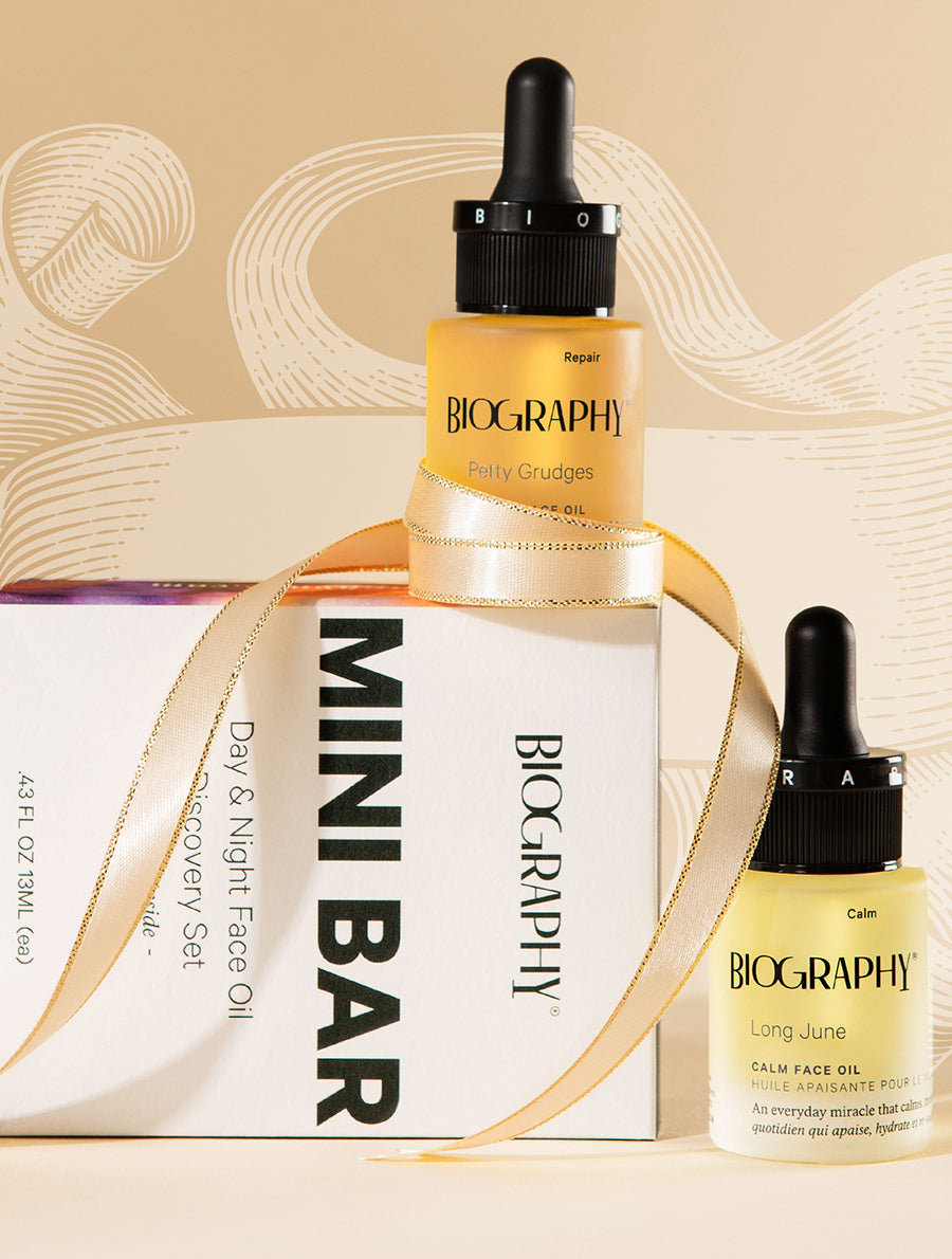 Two small glass bottles with dropper caps, labeled as part of a 'Mini Bar' gift set, with a yellow-toned liquid visible through the bottles, presented alongside a white box with branding elements.