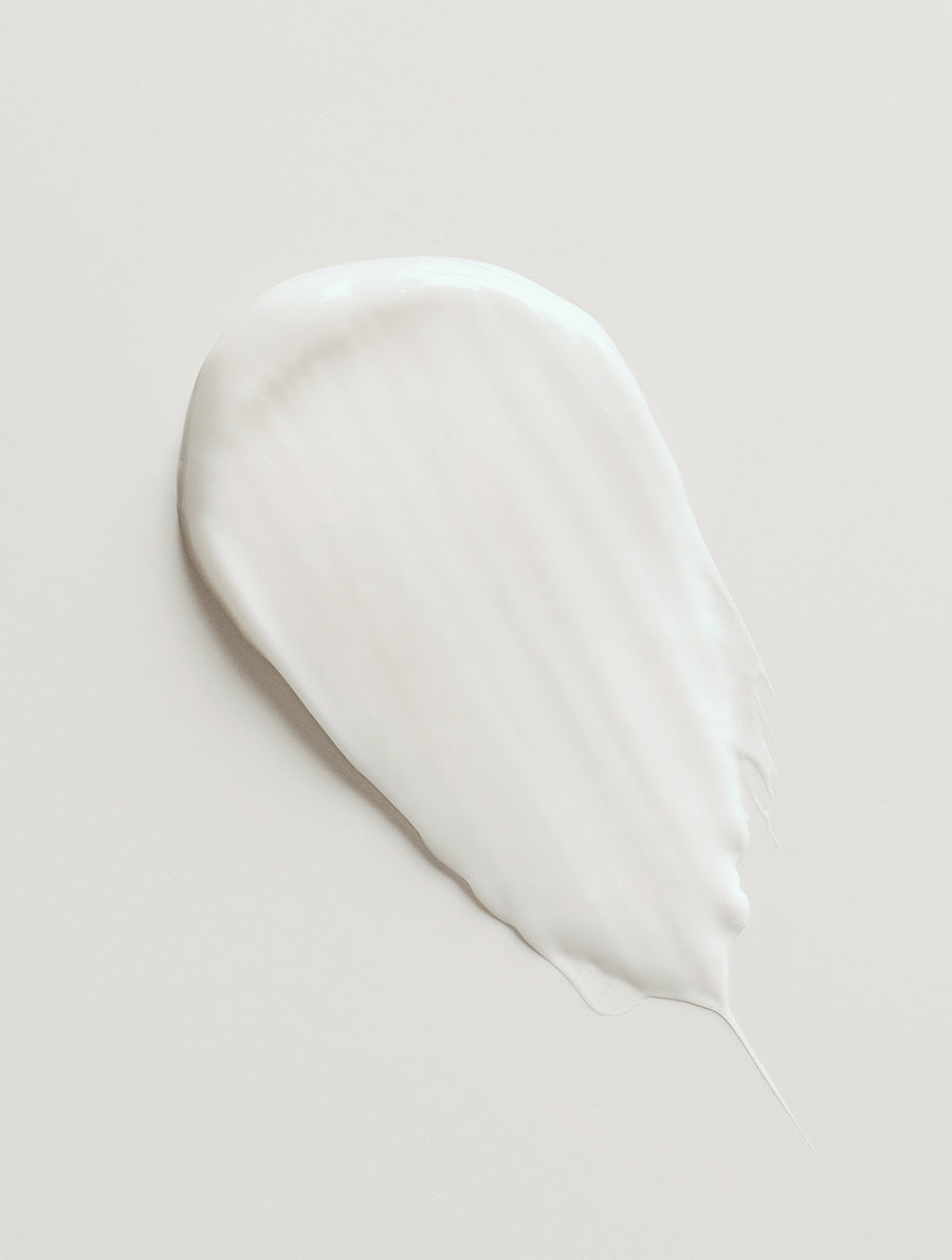 Close-up of a smooth, white pearlescent smudge showing the creamy texture and white color of our First Edition oil-infused hand and body cream on a neutral background
